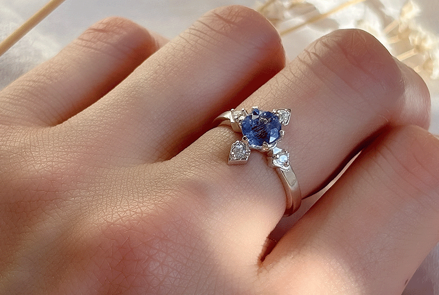 compassシリーズより、ブルーのカラーチェンジフローライトが中石のCelestiaを指に着用している写真。